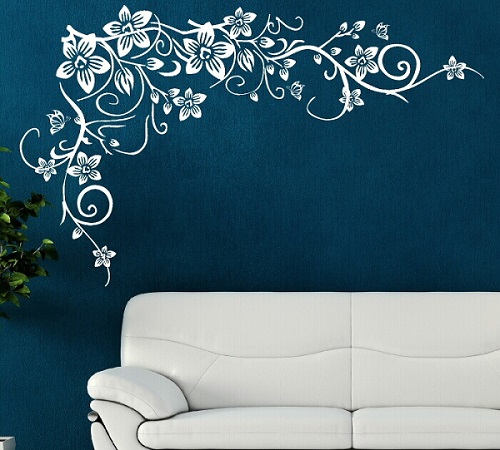 a white couch next to a dark blue wall with a white stencil flower pattern